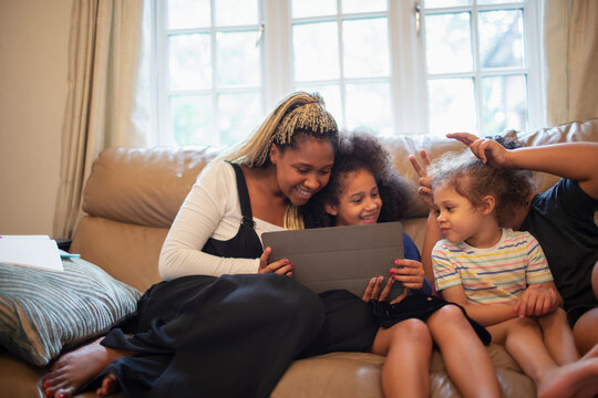 Mother and daughters using digital tablet on living room sofa