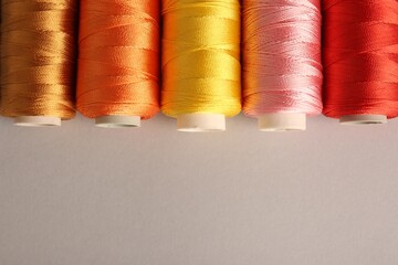 Different colorful sewing threads on light grey background, flat lay. Space for text
