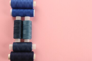 Different shades of blue sewing threads on pink background, flat lay. Space for text