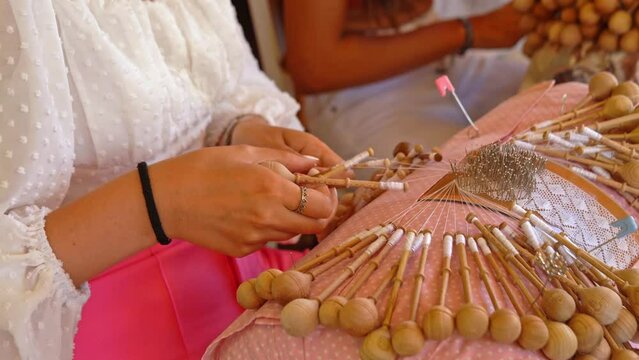 Bobbin lace handcrafting. Close-up of female hands braiding threads to make a pattern. Using threads and bobbins and needles according to the pattern.
