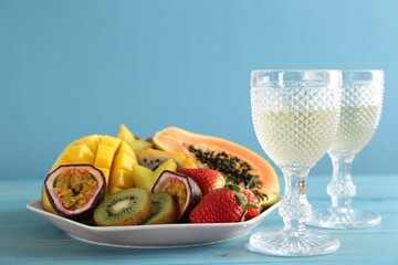 Delicious exotic fruits and glasses of wine on light blue wooden table