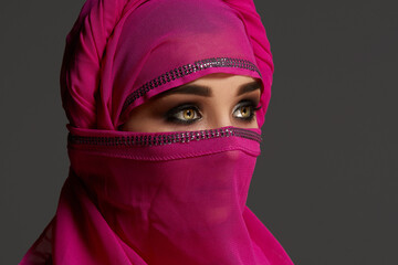 Close-up shot of a young charming woman wearing the pink hijab decorated with sequins. Arabic style.