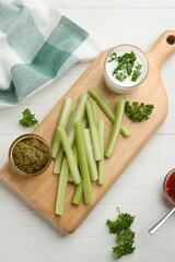 Celery sticks with different sauces and greenery on white wooden table, top view
