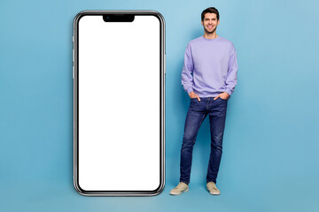 Full body photo of hr millennial brunet guy stand near ad wear sweater jeans sneakers isolated on blue background