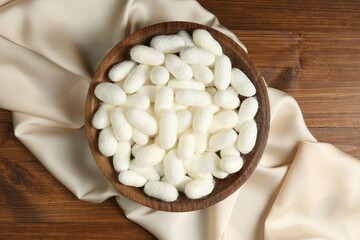 White cocoons with bowl and silk fabric on wooden table, flat lay
