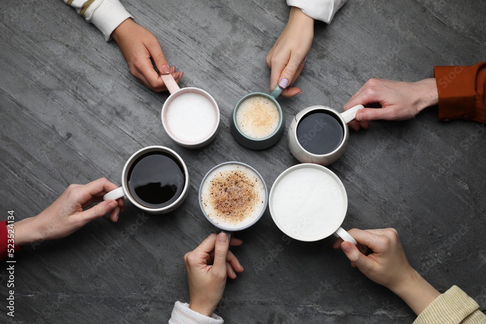 Wall mural People holding different cups with aromatic hot coffee at grey table, top view