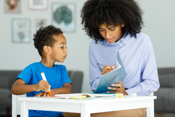  A young teacher helps a boy in elementary school lessons, shows a lesson in a book