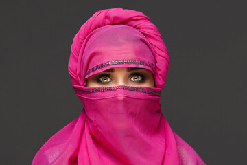 Close-up shot of a young charming woman wearing the pink hijab decorated with sequins. Arabic style.