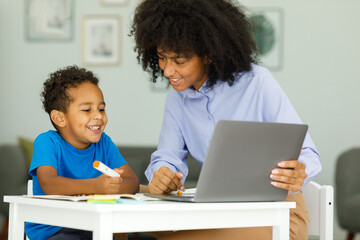 Portrait of cute african boy in using laptop with teacher, learning