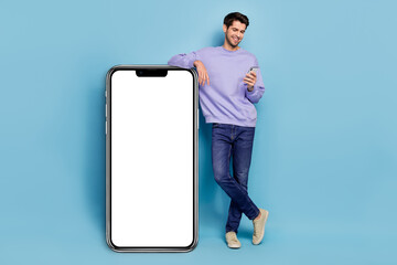 Full size photo of hr young brunet guy look telephone wear sweater jeans footwear isolated on blue background