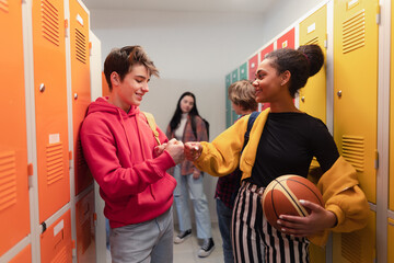 Young high school students meeting and greeting near locker in campus hallway talking and high fiving.