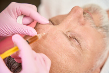 Cosmetologist through syringe injects beauty into man in beauty salon