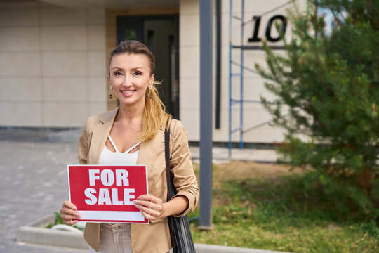 Woman realtor stands with sign in her hands for sale