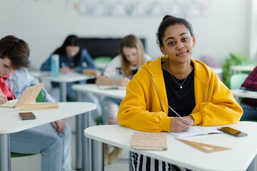 High school students paying attention in class, sitting in their desks and writing notes, back to school concept.