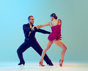 Dynamic portrait of professional dancers in stage attires dancing ballroom dance isolated on blue...