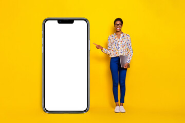 Full body photo of cheerful person indicate finger empty space large phone isolated on yellow color background