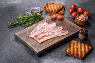 Raw smoked bacon slices on a wooden board with spices and herbs