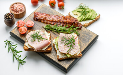 Fresh, delicious ham, butter, avocado and sesame seeds sandwiches on a wooden cutting board
