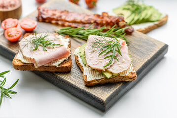 Fresh, delicious ham, butter, avocado and sesame seeds sandwiches on a wooden cutting board