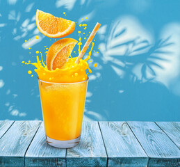 Glass of orange juice with orange splash on the table and stucco pattern wall with leaf shadows at the background.
