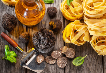 Black edible winter truffle, tagliatelle and fresh basil on wooden table. The most popular cooking ingredients.