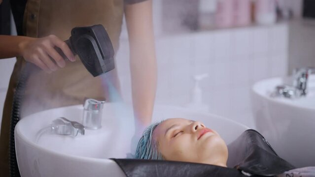 Caucasian young woman get hair washed by hairdresser stylist in salon. Beautiful customer girl lying down on salon washing bed feeling relax and happy enjoy massaging her head at beauty barber shop.