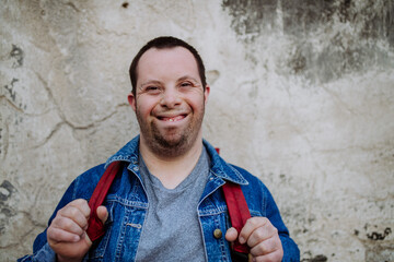 Portrait of happy young man with Down sydrome with backpack in street, smiling.