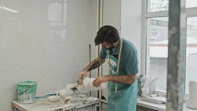Handheld shot of young adult Caucasian man with beard on face polishing plaster cast for socket detail with sandpaper in prosthetic production workshop