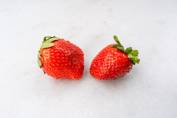Two red ripe strawberries on a white marble table surface, light background, top side view, healthy food, natural vitamins