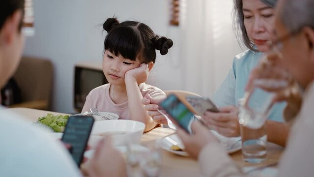 Asian family using phone while eating food not attention to girl kid. Upset daughter looking to addicted parents and grandparents using smartphones while eat breakfast. Family and social issue concept