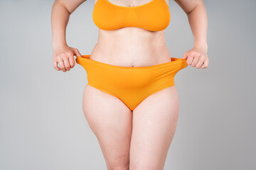 Fat woman in orange underwear on gray background, overweight female body