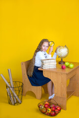 A blond schoolgirl sits at a desk with a magnifying glass in her hands on a yellow background....