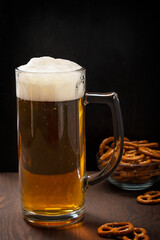 Organic craft cold wheat beer alcohol beverage served in drinking glass with dense foam or froth and crunchy salted snack crackers on dark brown wooden table at bar or restaurant for refreshment
