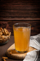 Homemade kvass fermented cereal-based low alcoholic beverage with light-brown colour and sweet-sour taste served in glass with salted crunchy croutons or dry bread as snack on dark brown wooden table