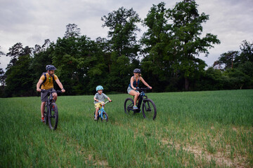 Fototapeta premium Young family with little child riding bicycles on meadow in village in summer.