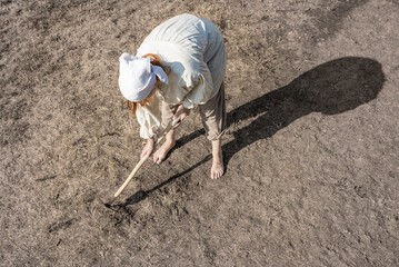A farmer desperately tries to work her dry field in summer.