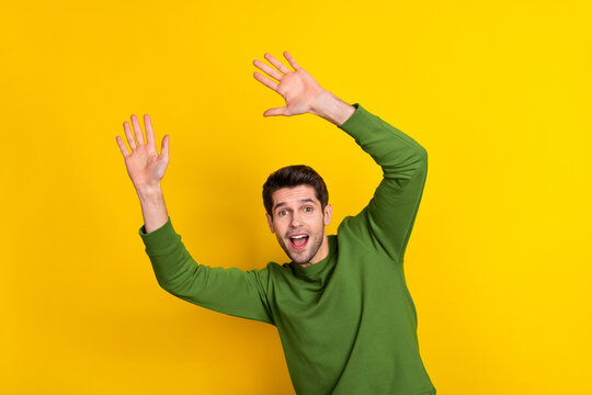 Photo of cute impressed young guy wear green sweater rising arms catching ball isolated yellow color background