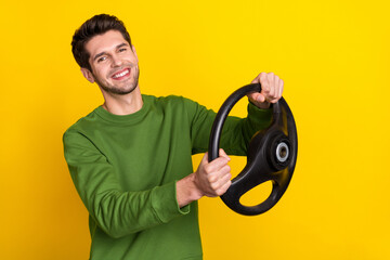 Portrait of attractive cheerful guy holding steering wheel riding isolated over vivid yellow color...