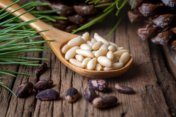 Pine nuts in the spoon and pine nut cone on the wooden table. Organic food.