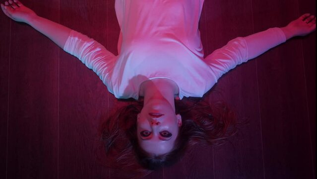 Mad woman lying on floor and looking at camera. Portrait of mysterious woman in darkness. Strange female. 4K, UHD