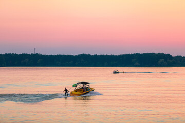 A boat pulls a person over the waves on a wakeboard. Wakeboarding at sunset
