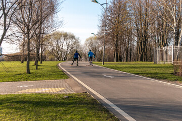 Biathletes in helmets ride roller skis in the park. Roller ski training. Adult men ride roller skis. Roller sports. The concept of competition, biathlon and training.