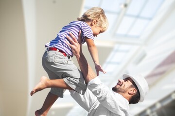 Obraz premium Happy daddy holding kid in arms, hugging toddler. Enjoying being father, spending time and playing with cute preschooler son, talking to child, laughing. Parent concept