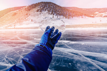 Tourist hand holds crystal clear heart made of ice from frozen Lake Baikal, sun light