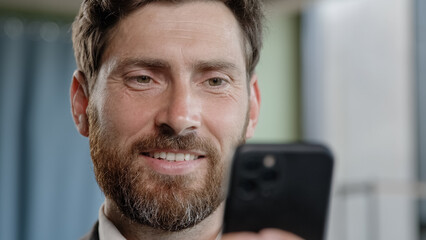 Obraz premium Close up head shot smiling bearded adult 40s businessman holding smartphone in office smile reading good news using online app middle-aged manager with cell phone mobile service texting corporate chat