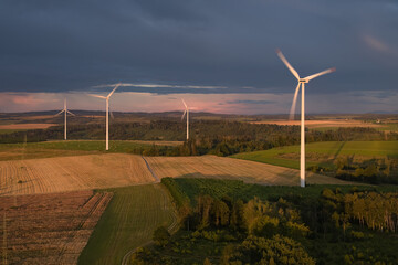 Aerial view of wind turbine farm. Wind power plant in full load illuminated with dramatic light against sunset sky with stormy clouds. Aerial, drone inspection of wind turbine.