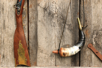 Stock of a traditional kentucky rifle and a gunpowder horn on an old, damaged board