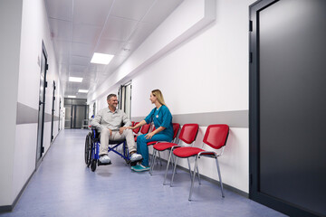 Man in wheelchair communicates with female doctor in corridor outpatient clinic