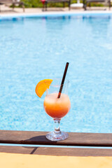 Fresh glass of a cocktail with an orange slice on the border of a swimming pool. Holiday and vacation concept.