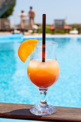 Fresh glass of a cocktail with an orange slice on the border of a swimming pool. Holiday and vacation concept.